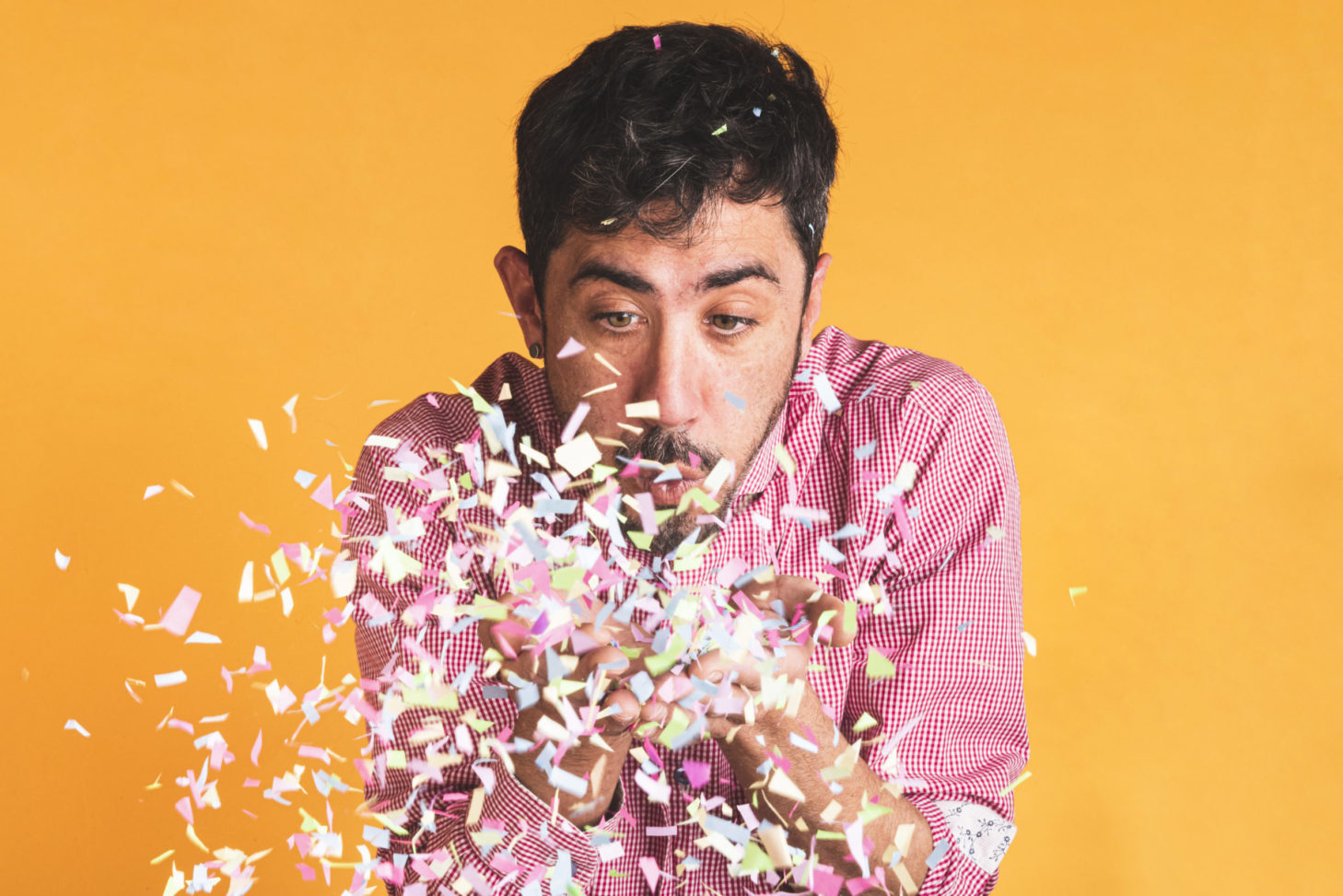 man-blowing-confetti-orange-background